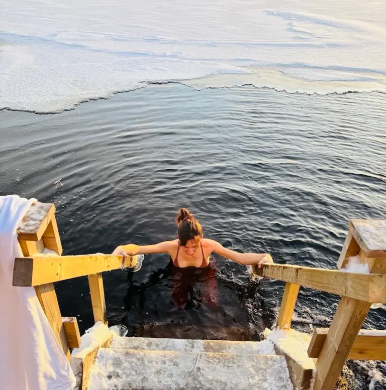 9 Winter Adventures in Lapland You Will Love - Around Europe Travel Blog a person going into a frozen lake after sauna in lapland