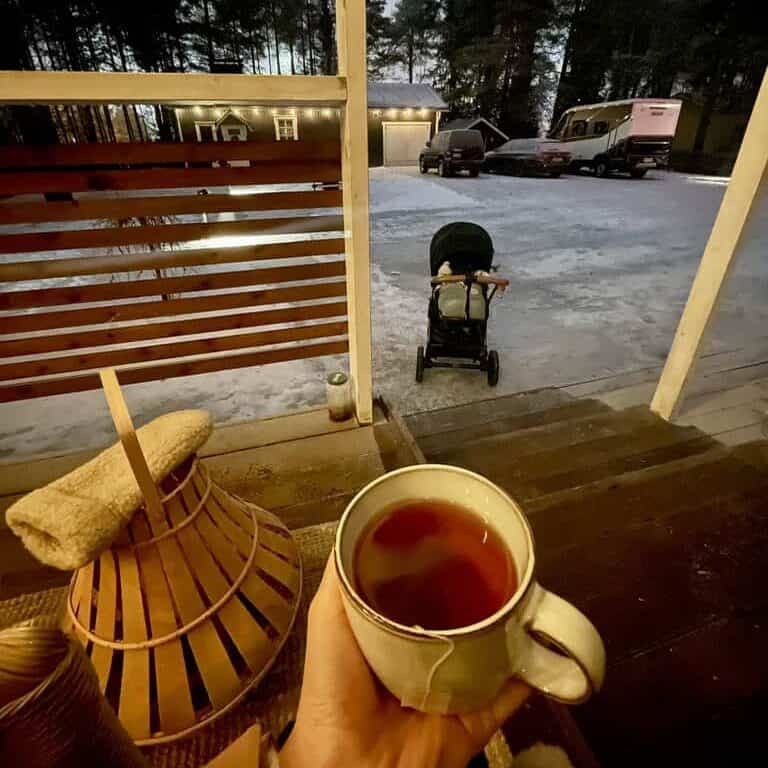 Baby napping in a stroller outdoors in the snow in Rovaniemi, with a cup of tea in the foreground